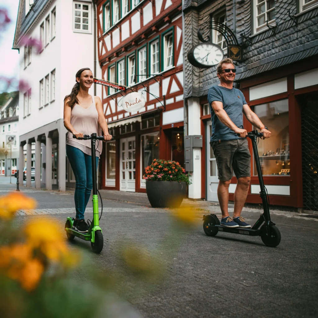 Zwei Personen mit STREETBOOSTER Vega E-Scootern in einer Altstadt